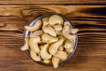 Glass bowl with raw cashew nuts on a wooden table. Top view