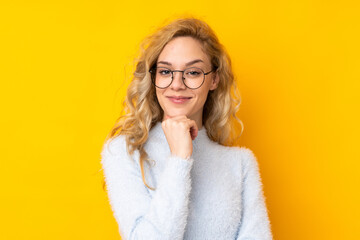 Young blonde woman isolated on yellow background with glasses and smiling