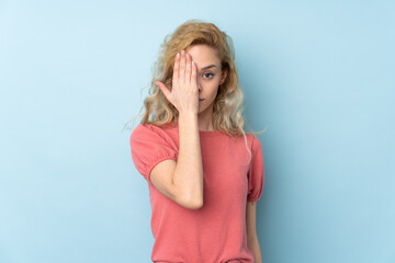 Young blonde woman isolated on blue background covering a eye by hand