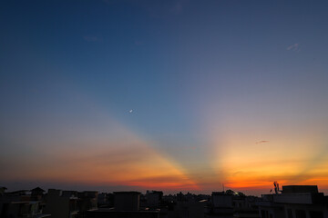 A breathtaking view of a city captured during sunset with colorful clouds and moon