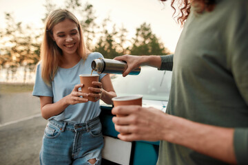 Man pouring coffee or tea from thermos flask, Attractive young woman drinking hot coffee or tea after repairing broken car on the road side - Powered by Adobe