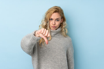 Young blonde woman wearing a sweater isolated on blue background showing thumb down with negative expression