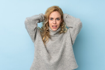 Young blonde woman wearing a sweater isolated on blue background frustrated and takes hands on head