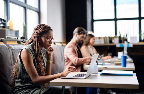 Portrait of young businesspeople with laptop working indoors in office.