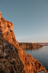 Orange stones rock in the light of the setting sun, by the bay with the coast on lake Baikal,
