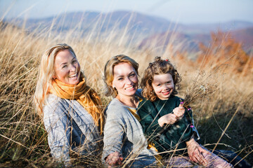Small girl with mother and grandmother resting in autumn nature.