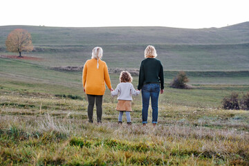 Rear view of small girl with mother and grandmother on a walk in autumn nature.