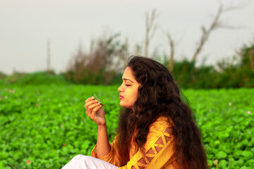 A beautiful Indian woman sitting with a leaf of a plant in her hand studying it
