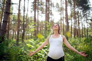 Portrait of happy pregnant woman outdoors in nature, doing yoga exercise.