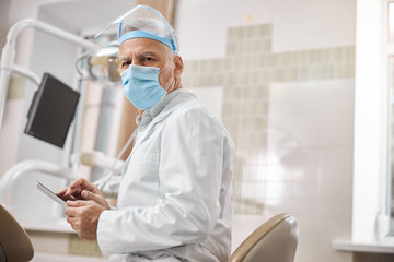 Professional senior dental specialist holding a tablet