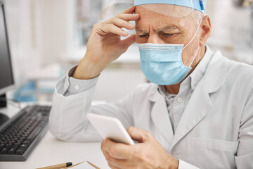 Aged medical doctor looking at his smartphone