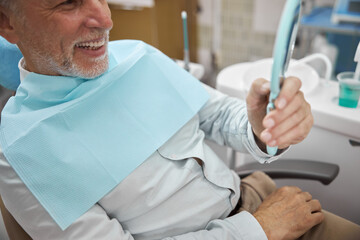 Eldelry patient looking at his teeth in the mirror
