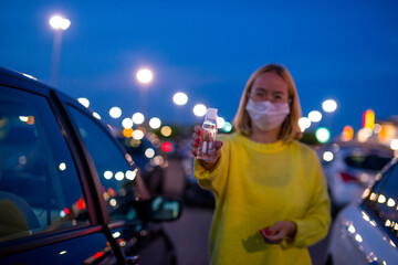 COVID-19 Pandemic Coronavirus Close up Woman Hands with Alcohol Gel Sanitizer with Young woman in a coronavirus mask in the background. Coronavirus concept. Nightlife