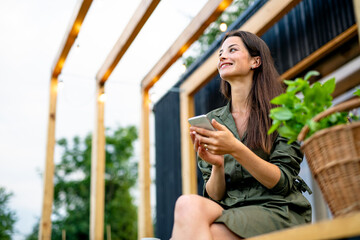 Young woman with smartphone outdoors, weekend away in container house in countryside.