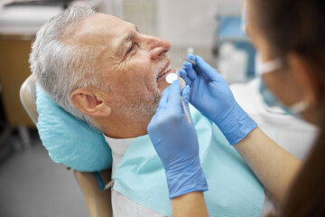 Obraz na płótnie Canvas Schooled young dentist examining an elderly patient