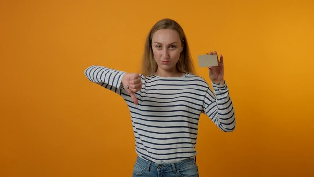 Young woman showing blank gray card, showing thumbs down gesture. The concept of bad shopping, substandard product. Yellow background. 4K video.