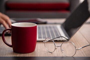 Glasses near cup hot coffee and laptop in background - work vibe concept