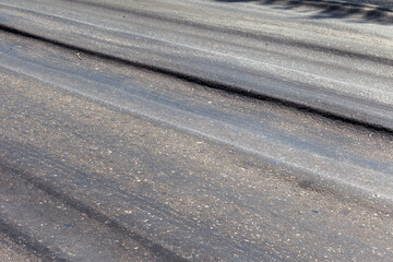 Damaged road, damaged chopped asphalt with potholes and spot. Very bad asphalt road with large trenche. Terrible technology of asphalt production in construction of road. Soft Asphalt melts from heat