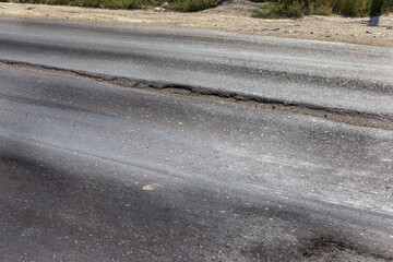 Damaged road, damaged chopped asphalt with potholes and spot. Very bad asphalt road with large trenche. Terrible technology of asphalt production in construction of road. Soft Asphalt melts from heat