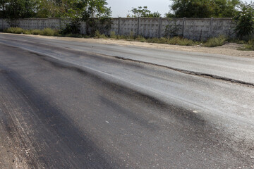 Damaged road, damaged chopped asphalt with potholes and spot. Very bad asphalt road with large trenche. Terrible technology of asphalt production in construction of road. Soft Asphalt melts from heat