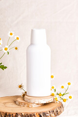 Fototapeta na wymiar Bottle of Mockup cosmetic products with chamomile flowers. Shampoo or mouthwash on wood slice. Beige fabric background