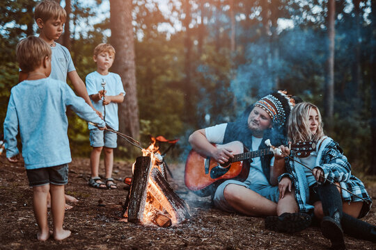 Loving couple with their boys camping and playing guitar near bonfire. Boys cooking treats and listening for music that playing their dad.