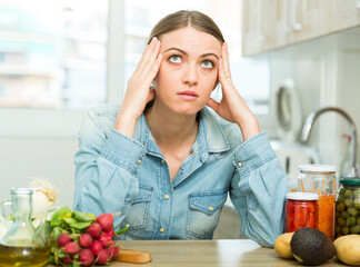 Portrait of upset young woman housewife sitting at home kitchen before cooking