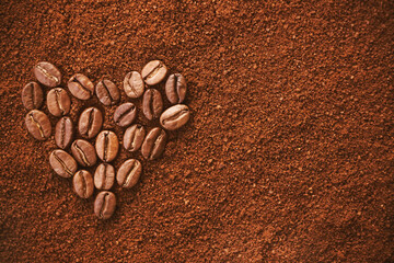 On the background of ground coffee, the heart symbol is laid out with roasted aromatic coffee beans. Love of coffee. Favorite invigorating drink.