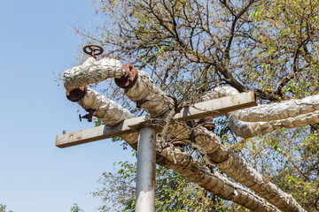 Overground heat pipes. Pipeline above ground, conducting heat for heating city. City aerial overground heating main in metal thermal insulation in residential city quarter. Open laying mains on poles