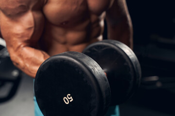 Athletic young man exercising with dumbbells at the gym