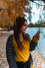 Vertical shot of a young woman touching a hanging leaf at autumnal park with a lake