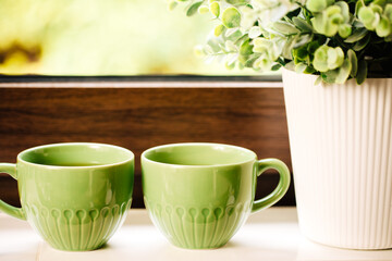 Two green cups with tea stand on a white windowsill next to a plant.