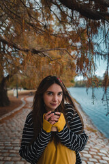 A pretty caucasian woman holding a cup of coffee to go at autumnal park. Vertical, copy space