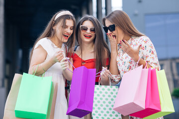 Successful shopping. Casual makeup. A group of young happy cute woman in casual dresses, top and pants walking from the building with yellow, green, purple and pink bags in their hands