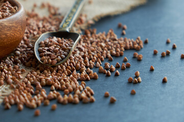 Fototapeta na wymiar Buckwheat groats in a wooden bowl and vintage scoop. Close up on a black background. copy space for text