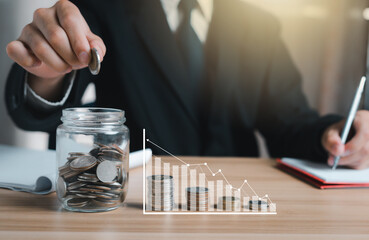 Businessman making stack of coins holding coin put into the jar and there is a hologram to graph information about the growth of the business. Concept saving money, technology business investment.
