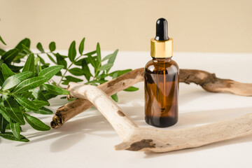 Brown bottle with cosmetic product on a natural beige background made of branches and green leaves.