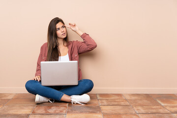 Teenager student girl sitting on the floor with a laptop making the gesture of madness putting...