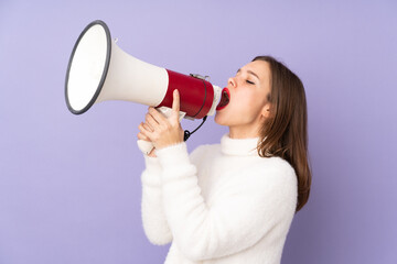 Teenager girl isolated on purple background shouting through a megaphone