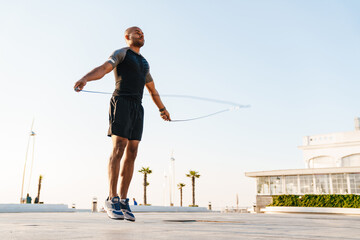 Image of athletic african american sportsman working out with jump rope