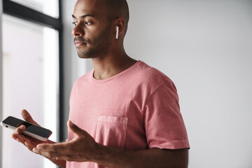 Image of young african american guy using mobile phone and earphone