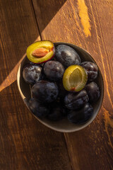 dark blue plum in a plate on a wooden table in the morning sun