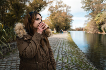 A pretty caucasian woman drinking a coffee while enjoying a walk at park. Copy space