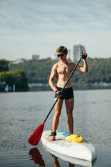 Portrait of sporty handsome man with sexy body rowing at sea standing on sup board. Vertical. Active summer vacation.