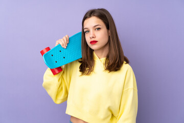 Teenager girl isolated on purple background with a skate © luismolinero