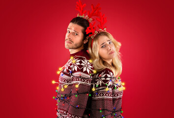 Unhappy millennial couple tied with Christmas lights over red background