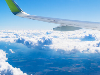 airplane wing in blue sky over rain clouds and land during flight on summer day