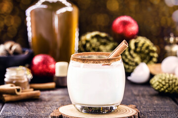 hot christmas drink with decoration and christmas lights in the background, called eggnog, made with sugar, nutmeg, cinnamon and alcoholic drink