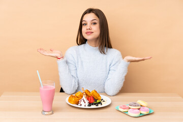 Teenager girl eating waffles isolated on beige background with shocked facial expression