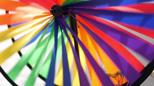 Colorful pinwheel spinning, weather wind vane, garden decoration in USA. Rainbow symbol of childhood, fantasy and imagination rotating. Multi colored spiral toy turning in breeze. Summertime dreaming